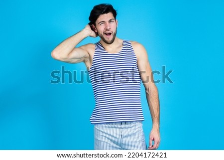Handsome Brunet Man in Striped Underware During Early Morning Yawing While Scratching His Heand From Behind Against Seamless Blue Background. Horizontal Image