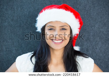 Closeup portrait of a cute Christmas woman with a red Santa Claus hat, white dress, head shot, smiling,celebration time. Positive human emotion on isolated grey background.