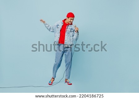 Full body young singer middle eastern man 20s he wear denim jacket red hat sing song in microphone at karaoke club isolated on plain pastel light blue cyan background studio. People lifestyle concept Royalty-Free Stock Photo #2204186725