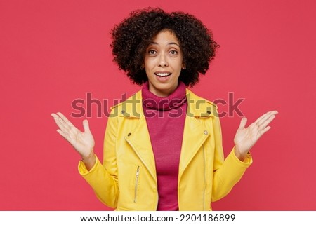 Charming bright happy young curly latin woman 20s years old wears yellow jacket looking camera spreading hands isolated on plain red background studio portrait. People emotions lifestyle concept