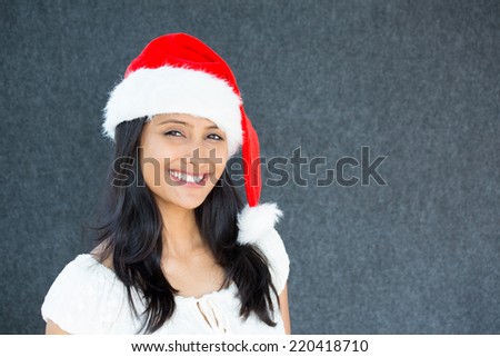 Closeup portrait of a cute Christmas woman with a red Santa Claus hat, white dress, smiling,happy, awaiting holiday season. Positive emotion on isolated grey background.