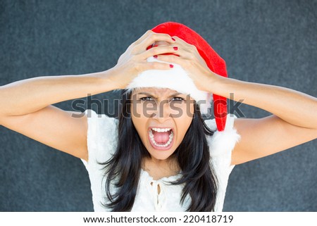 Closeup portrait of a cute Christmas woman with a red Santa Claus hat, white dress, hands on head, stressed out, yelling, showing frustration. Negative human emotions on isolated grey background. 