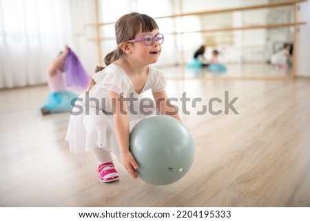 Little girl playing with ball at ballet class in dance studio. Concept of integration and education of disabled children. Royalty-Free Stock Photo #2204195333