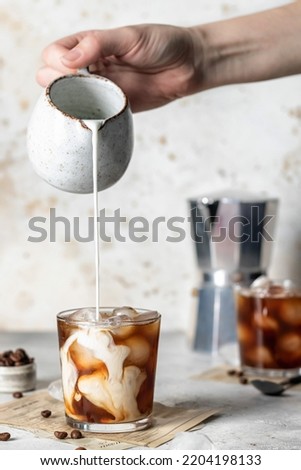 Pouring milk in coffee with ice cubes with beautiful twists on light background. Vertical orientation. Iced latte coffee still life Royalty-Free Stock Photo #2204198133