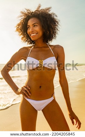 Healthy young African American girl in white bikini enjoying carefree lifestyle by the ocean on Summer beach vacation