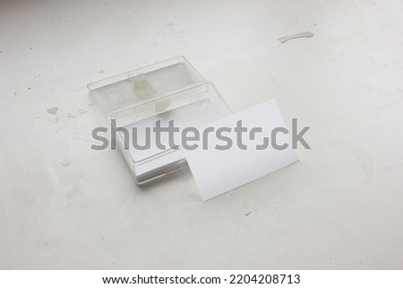 A set of blank business name cards in a transparent acrylic box with the standing one is isolated on white textured desk background for corporate identity mockup or stylish aesthetics presentation.