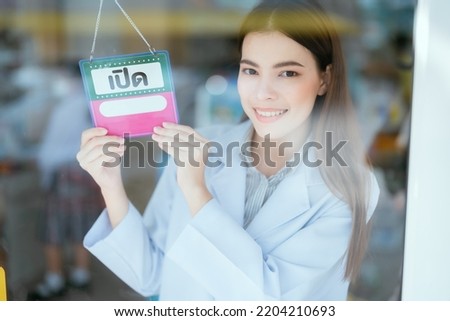 Pharmacist in front of a shop with an "open" sign in Thailand. looking out the glass window