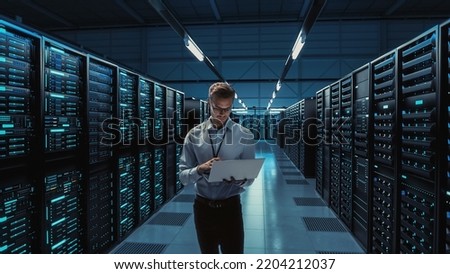 Futuristic Concept: Big Data Center Chief Technology Officer Holding Laptop, Standing In Warehouse, Information Digitalization Lines Streaming Through Servers. SAAS, Cloud Computing, Web Service Royalty-Free Stock Photo #2204212037
