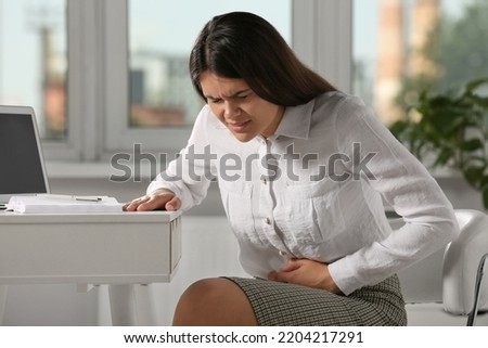 Young woman suffering from menstrual pain in office Royalty-Free Stock Photo #2204217291