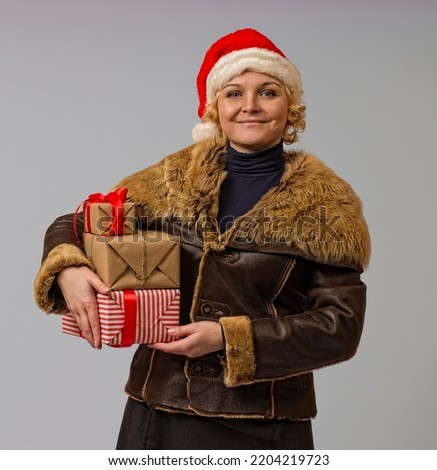 woman in a winter jacket and santa claus hat with boxes of gifts in her hands on a white background, close-up