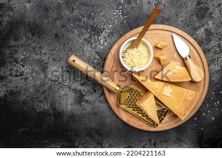 grated parmesan cheese and metal grater on a dark table, Parmesan is hard cheese uses in pasta dishes, soups, risottos and grated over salads. top view.