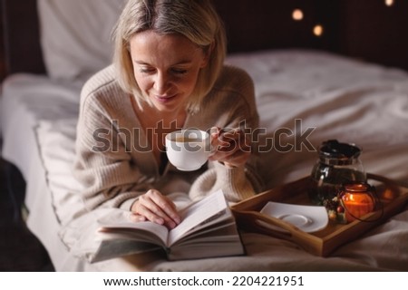 Adult attractive woman is reading book and drinking tea in her bedroom. Middle aged female lies on the bed and holds a book in her hands
 Royalty-Free Stock Photo #2204221951