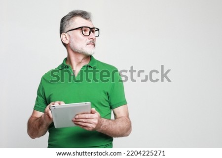 Photo of handsome mature man dressed green t-shirt and eyeglasses use tablet pc over light grey background