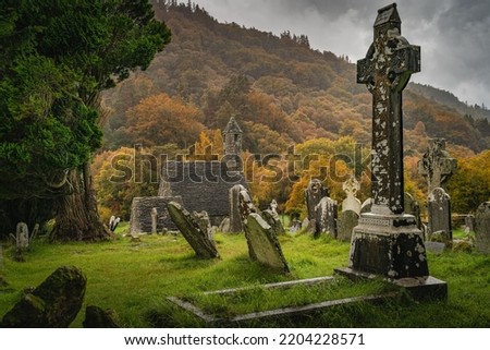 Medieval church ancient graves Celtic crosses in Glendalough Cemetery. Moody autumn forest, mountains in rain, storm sky in background Wicklow Ireland Royalty-Free Stock Photo #2204228571