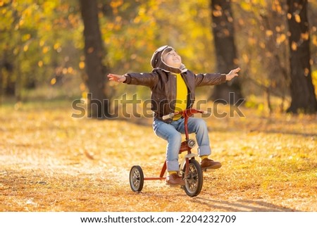 Portrait of happy child pilot against yellow leaves background. Funny kid riding bike outdoor in autumn park. Freedom and imagination concept Royalty-Free Stock Photo #2204232709