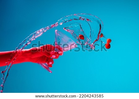Female hand spilling over Martini cocktail with cherries splashing over blue background in pink neon light. Nightlife, party. Hard drink. Concept of alcoholic drinks, party, taste. Food and drink art Royalty-Free Stock Photo #2204243585
