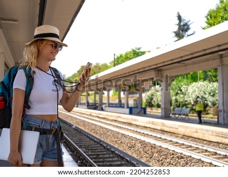 selective focus on Woman waits for train at station while working happily on phone, digital nomad, travel and transportation concept