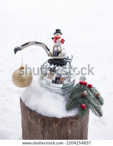 model of toy metal excavator, miniature snowman stand on mirror ball, Christmas ball for decorations hangs on arrow. concept of christmas business greetings in construction companies, winter