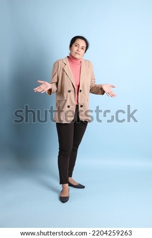 The senior Asian woman with pink shirt brown blazer on the blue background.