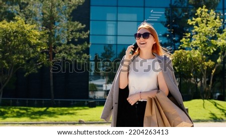 Modern business building beautiful smiling lady with sunglasses take her smartphone and speaking with someone in a beautiful sunny day