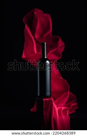 Bottle of red wine on a black background with flutters red cloth.