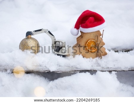 model of toy metal excavator and a gingerbread in form of Christmas tree in Santa hat standing on snow. concept of christmas business greetings in construction companies. winter holiday atmosphere