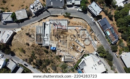 Top down view of a construction site from a drone with concrete and dirt tones and a winding street next to the site