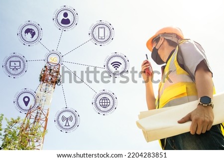 Team male architect engineers wearing masks helmets reporting on radio communications tower structure holds blueprints to monitor telecommunication signals, 5G networks internet data. Royalty-Free Stock Photo #2204283851