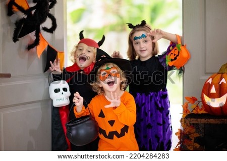 Kids trick or treat on Halloween night. Child at decorated house door. Boy and girl in witch and vampire costume and hat with candy bucket and pumpkin lantern. Autumn decoration. Friends play.