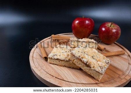 Apple pie with cinnamon. Apple pie, red apples and cinnamon on wooden round cake stand, close-up on black background