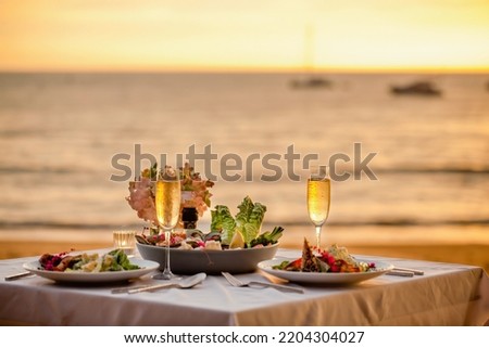 Romantic sunset dinner on beach. Table honeymoon set for two with luxurious food, glasses of champagne drinks in restaurant with sea view and yachts on background. Summer vacation or wedding concept. Royalty-Free Stock Photo #2204304027