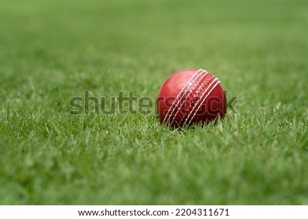 Closeup of a red cricket ball laying on a green grass