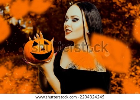 Autumn halloween photo of girl in autumn forest with pumpkin. Witch with tattoo costume for halloween. Brunette with makeup