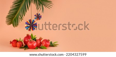 Pomegranates, palm leaves with colorful holiday decorations on a coral background, Rosh Hashanah and Sukkot concept. Banner with space for text Royalty-Free Stock Photo #2204327599