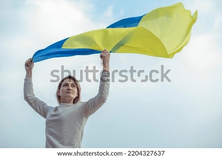 Woman girl holding Ukrainian flag  flying in the wind against the sky 