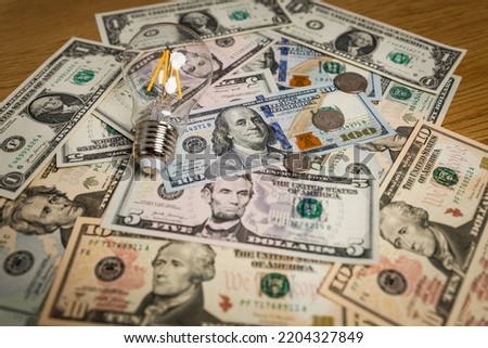 Classic electric light bulb with money scattered on the desk. Photo for Finance and energetic and high electricity bill prices concepts. 
 World economy crisis.