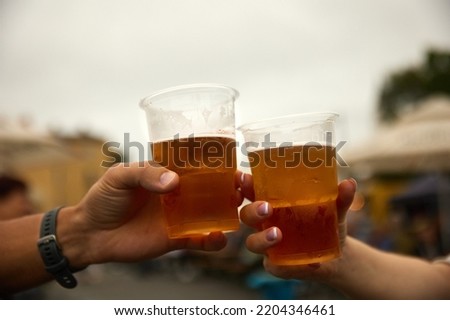 Friends clink glasses with light beer on the street Royalty-Free Stock Photo #2204346461