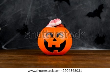 Trick ot treat concept. Halloween background with Jack-o-Lantern shaped candy bowl full of sweets against spooky decorated wall.