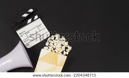 White clapper board and megaphone and a box of popcorn on black background.	


