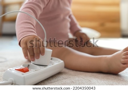 Cute baby playing with charger and power strip on floor at home, closeup. Dangerous situation Royalty-Free Stock Photo #2204350043