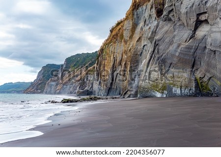 Sheer White Cliffs of the Pacific coast of northern Taranaki. Thin layer of water on smooth sand reflects the sky. Low tide in the Pacific Ocean. The magnificent nature of New Zealand. 