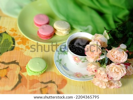 A cup of coffee, macaroons, and a bouquet of pink roses on a green chiffon background, a festive arrangement of horizontal orientation with sweets, top view.