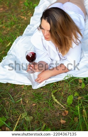 Portrait of a beautiful woman lying on the grass in a white shirt and openwork panties with a glass of wine