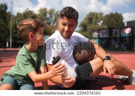 Father and son taking a break after playing a game of basketball. Young man and teenage boy talking and drinking water