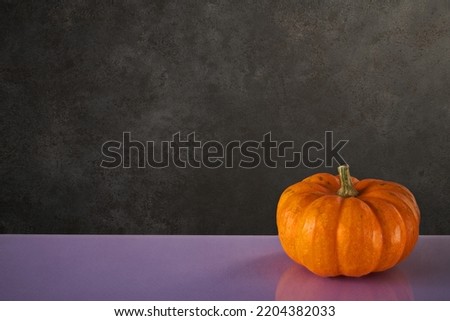 Pumpkin on the table and a black stone background. Colorful autumn pumpkin postcard with space for text, good for halloween. High Resolution, detailed photography.