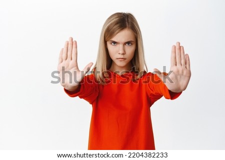 Serious little girl showing stop, prohibition taboo gesture, extending arms and blocking smth bad, rejecting, standing over white background.