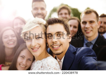 Young couple of newlyweds with group of their firends taking selfie