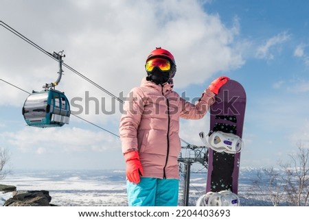 A snowboarder at the top of a ski slope with a snowboard in his hands. On the background of a ski lift. 