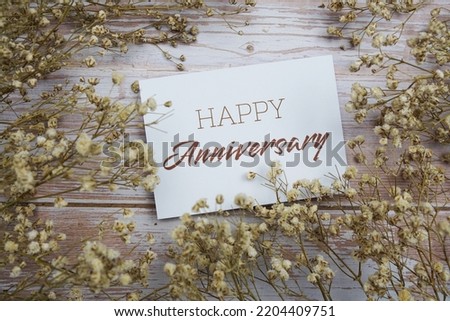Happy Anniversary text on paper card with flower decoration on wooden background