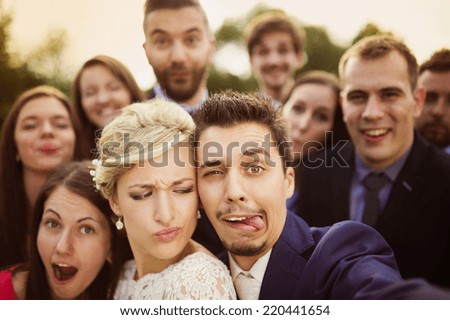 Young couple of newlyweds with group of their firends taking selfie and making funny grimaces